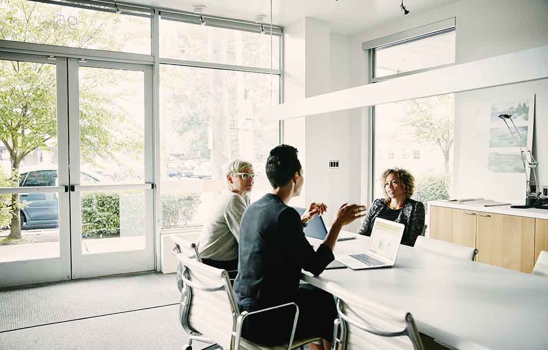 Business professionals sitting at a conference table discussing with one another.