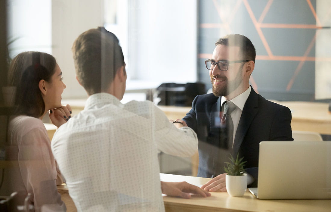 A couple shaking hands with a business professional in a suit.