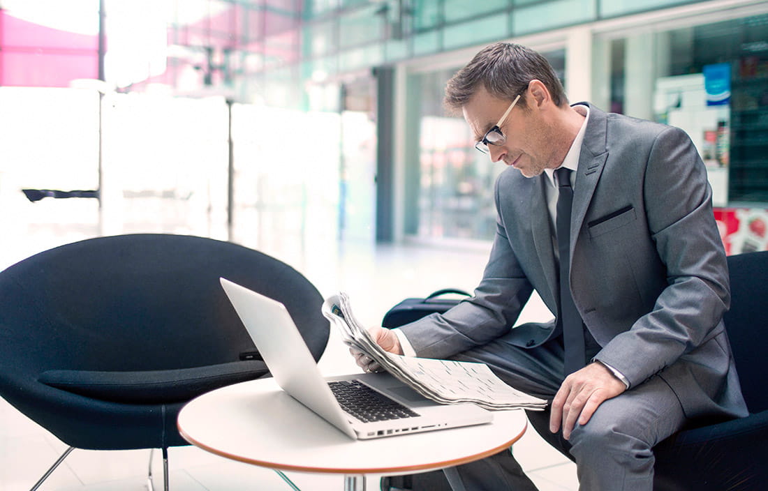 Business man looking at his newspaper and laptop.